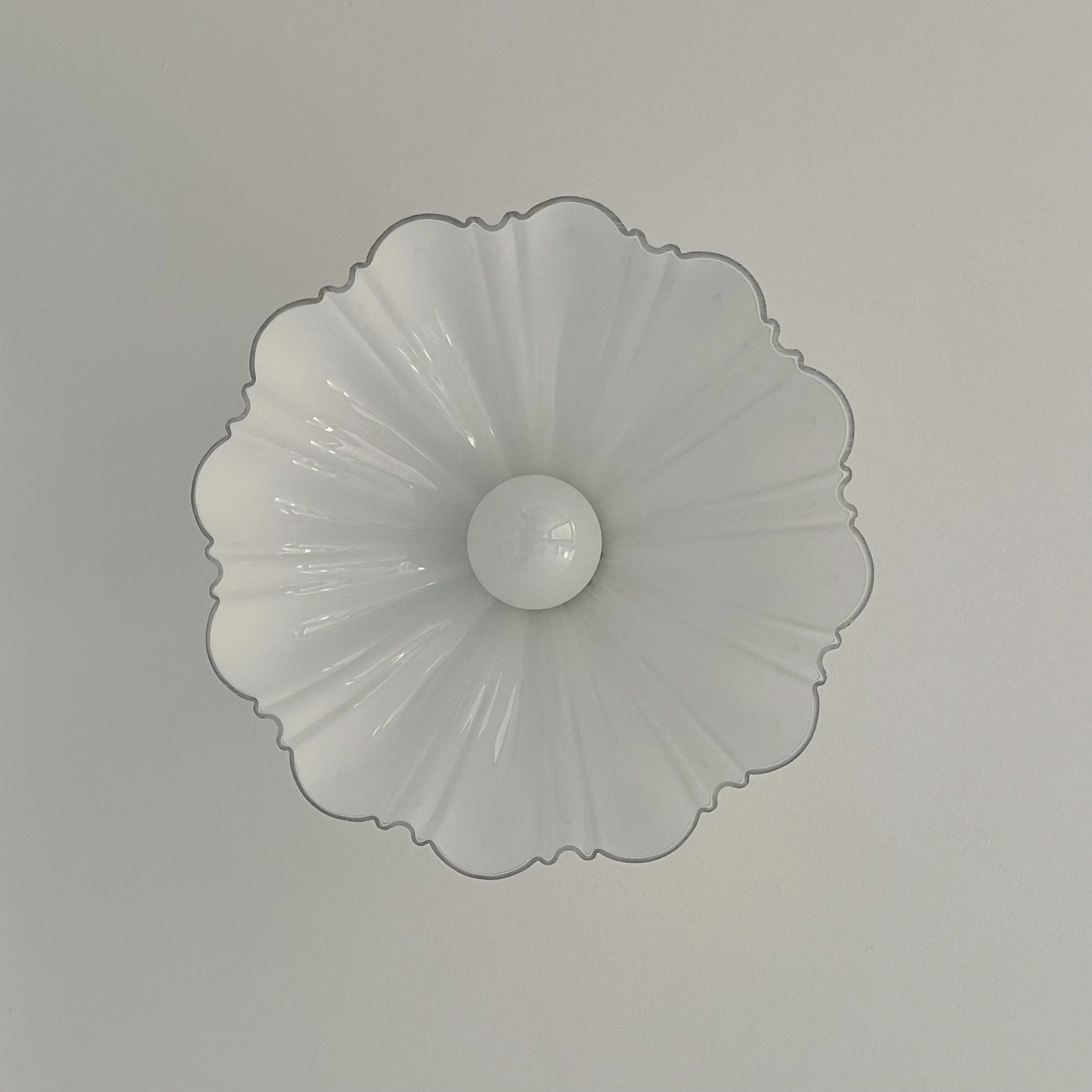 Ceiling light fixture with a round white bulb and a decorative glass shade with wavy edges and radiating lines.