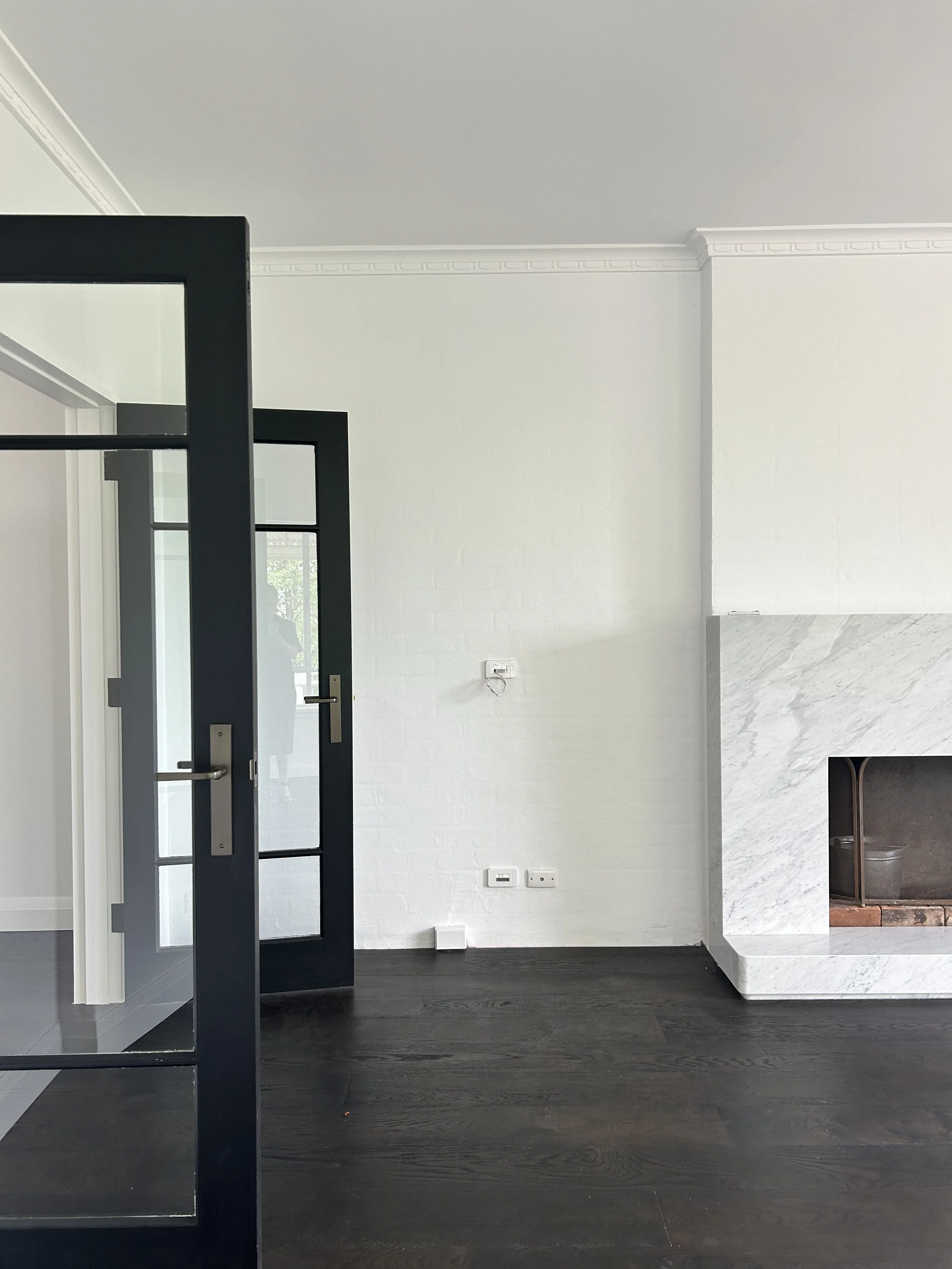 Interior of a modern room with white walls, dark hardwood floors, a white marble fireplace, and black-framed glass doors.