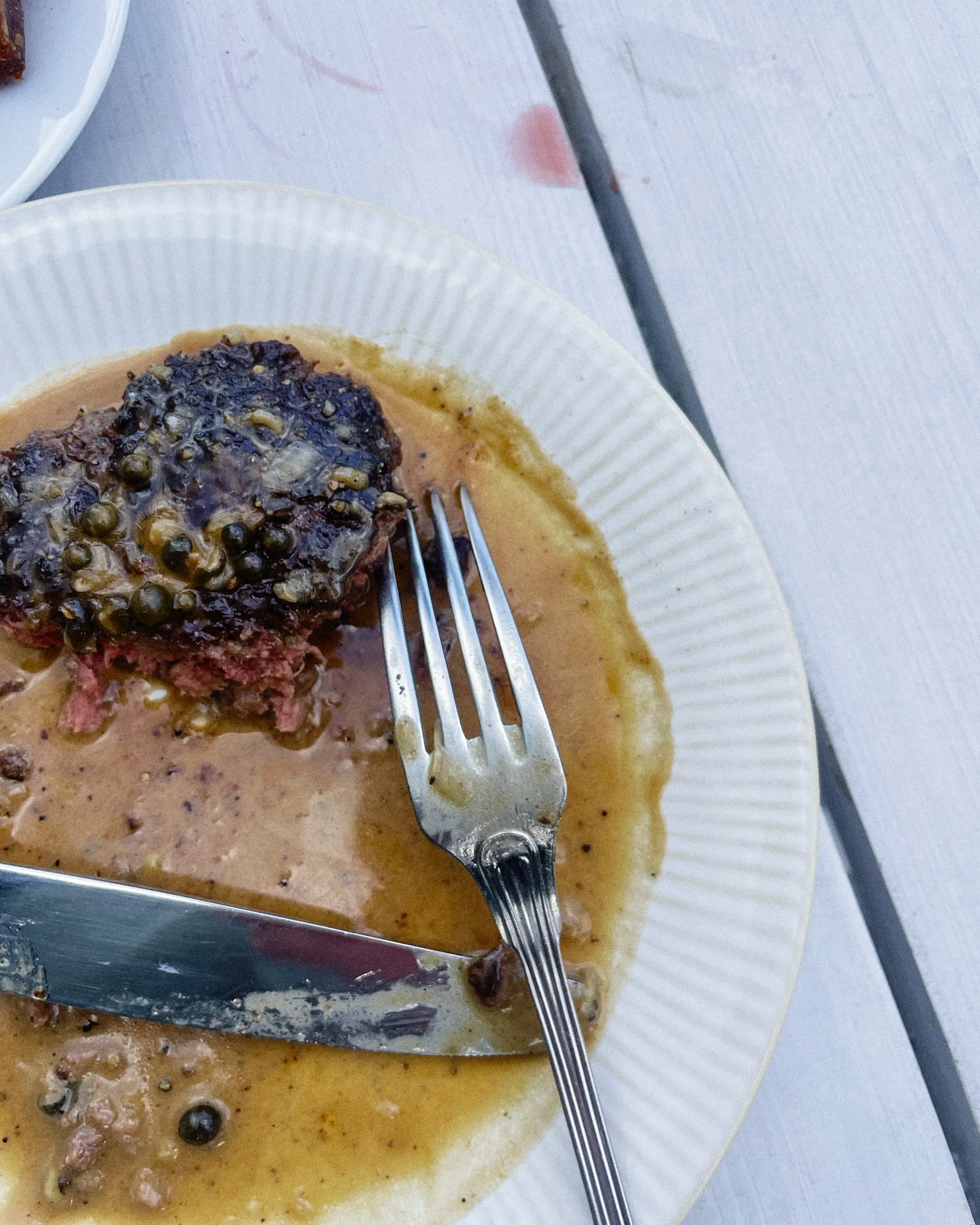 Steak with peppercorn sauce on a white plate, accompanied by a fork and knife.