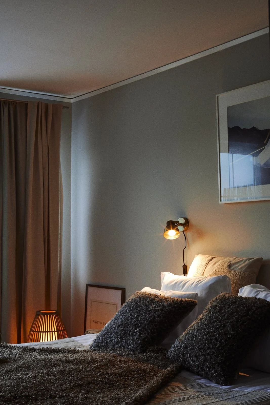 Cozy bedroom with a bed, decorative pillows, a wall-mounted lamp, framed artwork, and soft lighting.