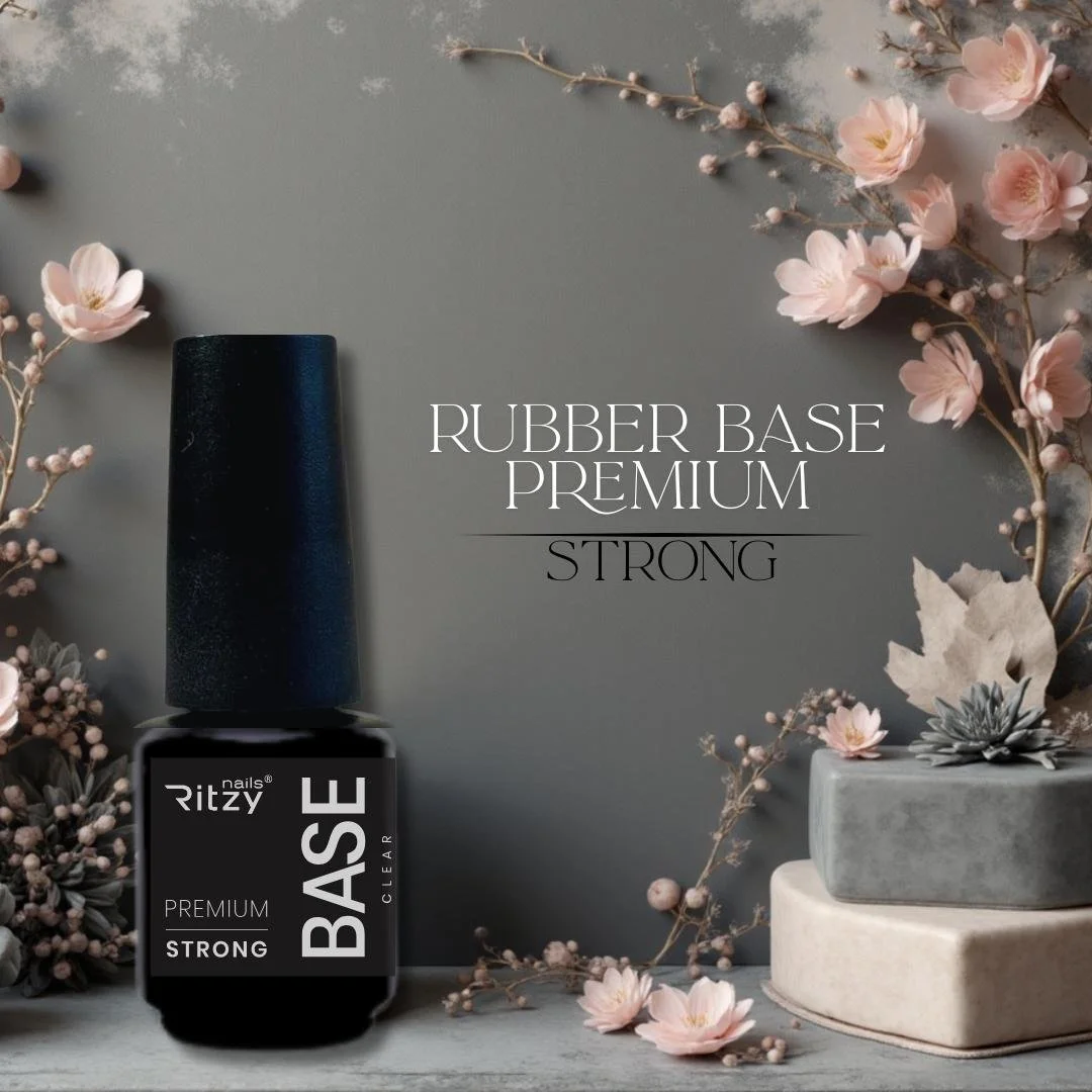 A bottle of Ritzy nail polish with a black cap on a surface decorated with pink flowers and gray and white stone blocks, with text reading 'Rubber Base Premium Strong'.
