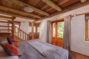 A yoga class taking place in a wooden pavilion. Several people are seated on yoga mats, facing a yoga instructor. The setting is natural with trees visible through open sides. Participants are using props like yoga blocks and bolsters.