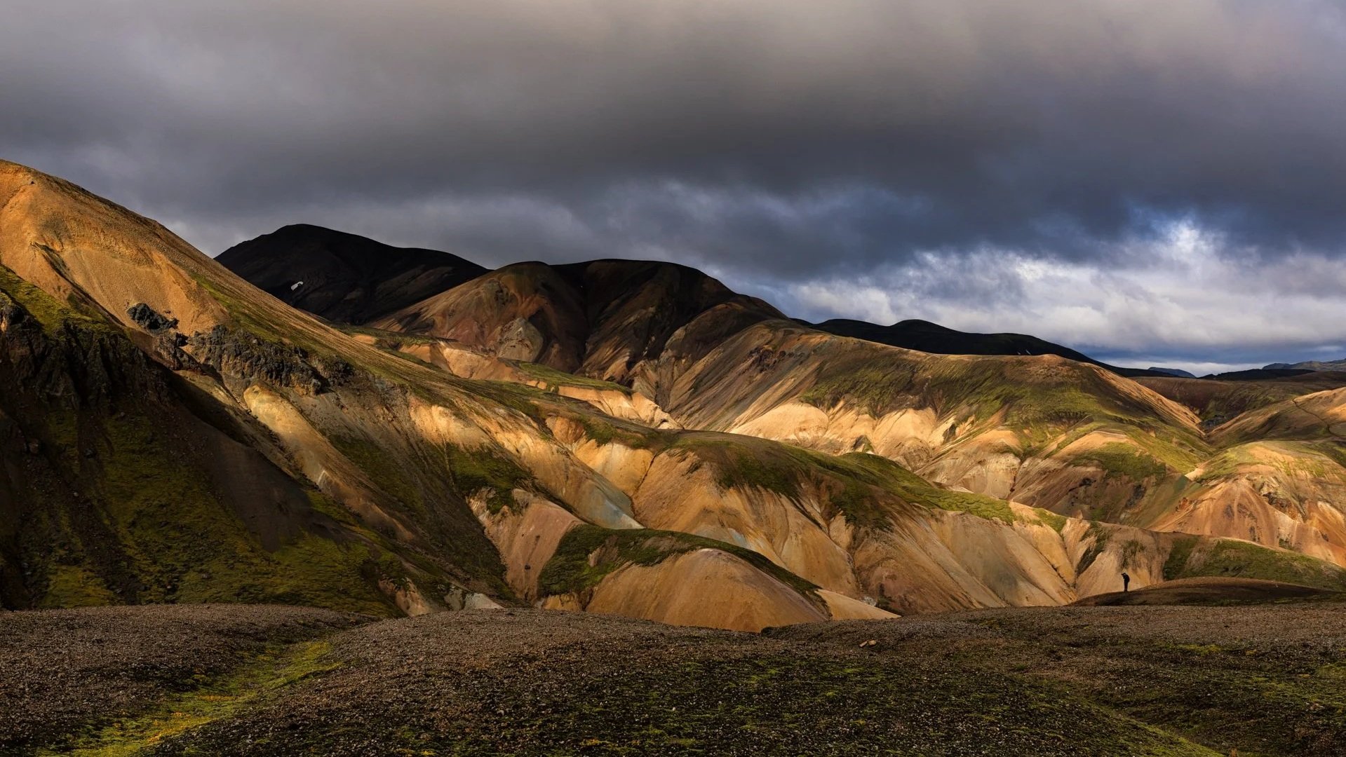 Bunte, bergige Landschaft unter einem dunklen, bewölkten Himmel