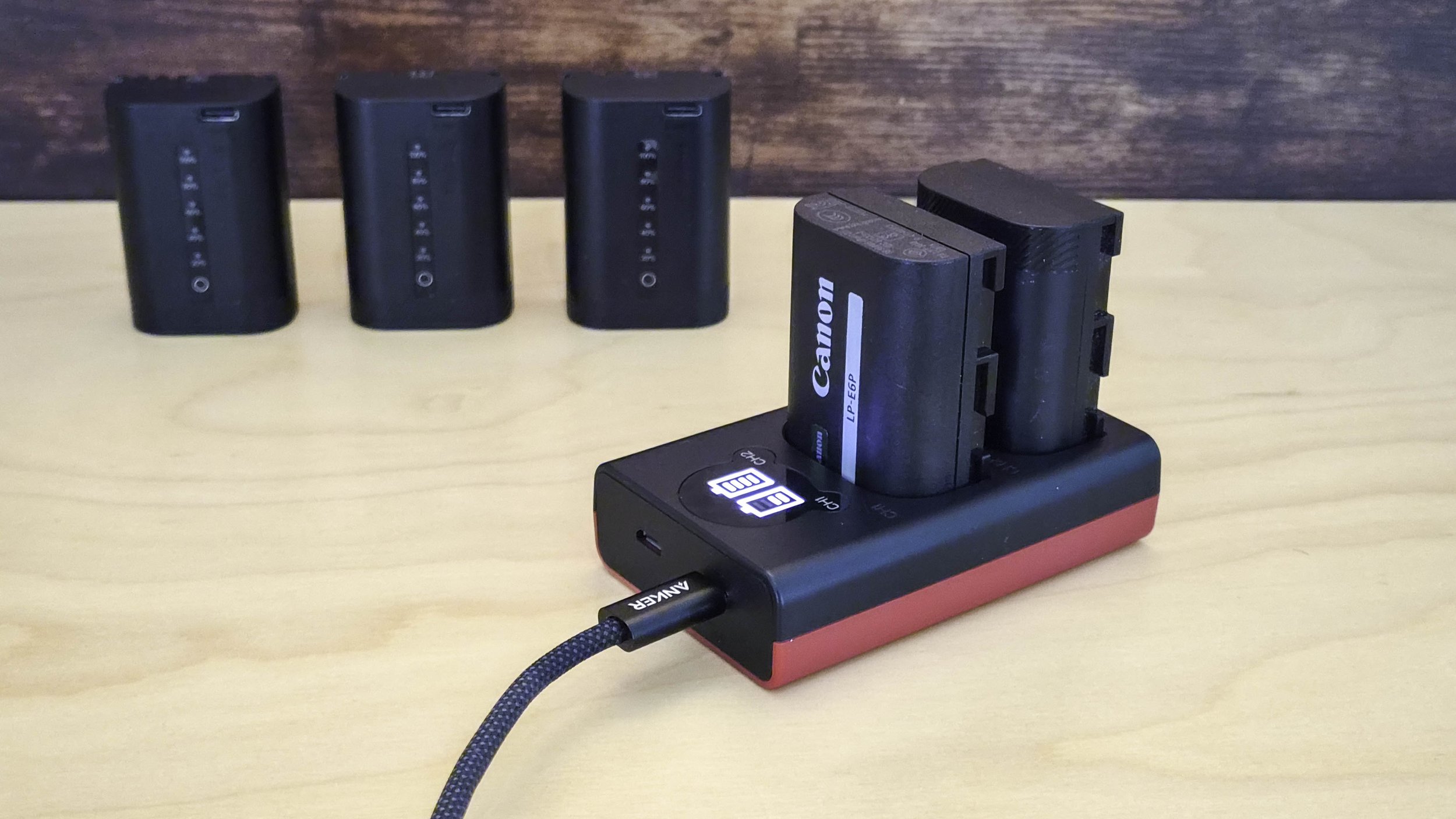 Zwei LP-E6P Akkus werden in einem Baxxtar Ladegerät über USB geladen. Im Hintergrund weitere Akkus.