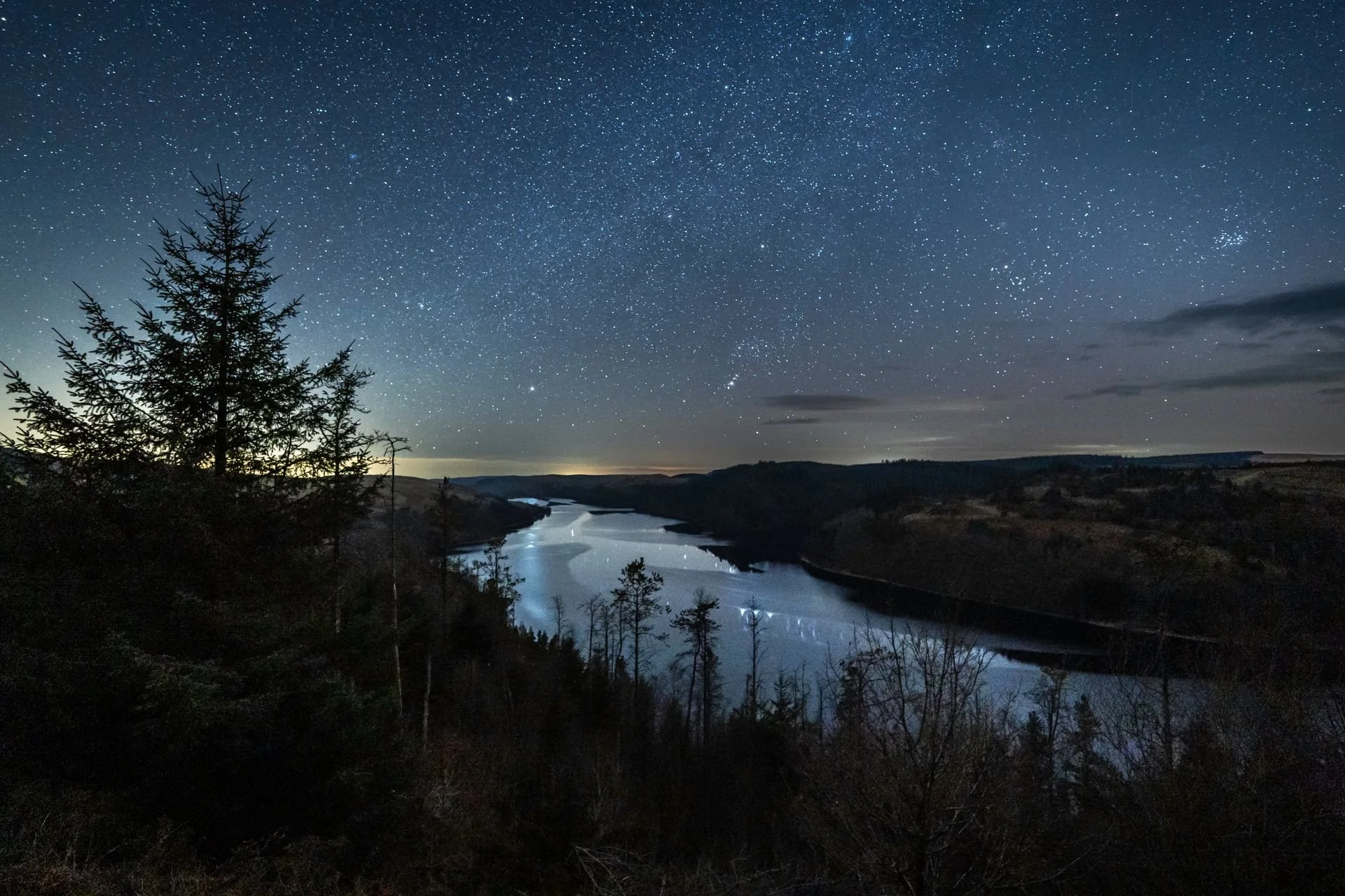 Nighttime landscape of a river winding through wooded hills under a star-filled sky.