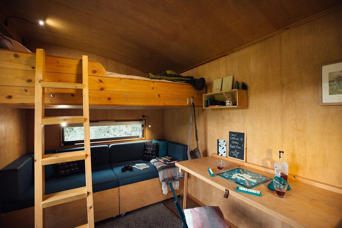 Cabin bed with ladder inside Hafan, table and chairs area to right, and sofa and pull out bed underneath, all in timber.