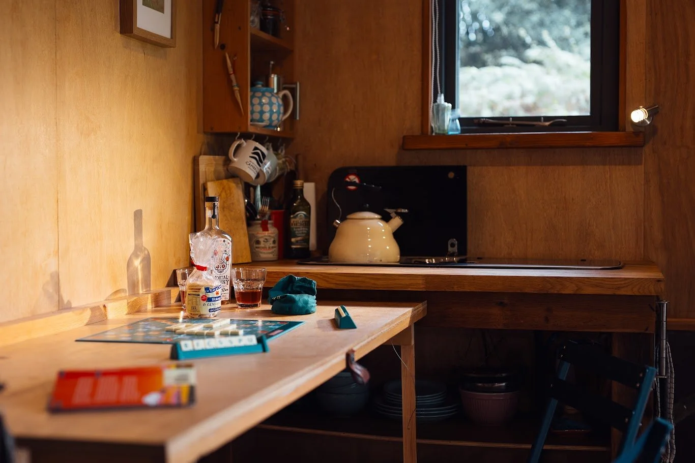 Detail of the kitchen and dining corner of Hafan Cabin with leaflets, glasses, a bottle, stove, cups and kettle.