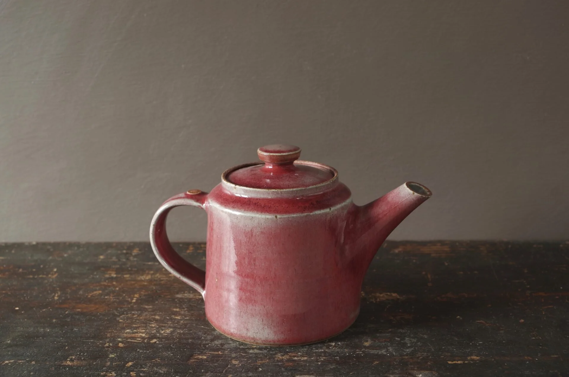 Red teapot made by James & Tilla Waters. Thrown stoneware teapot with pulled handle and copper red glaze.  Beautifully made and lovely to use.  Unglazed thumb dot and knob edge.  Unglazed base with makers mark.  Capacity approx. 650ml