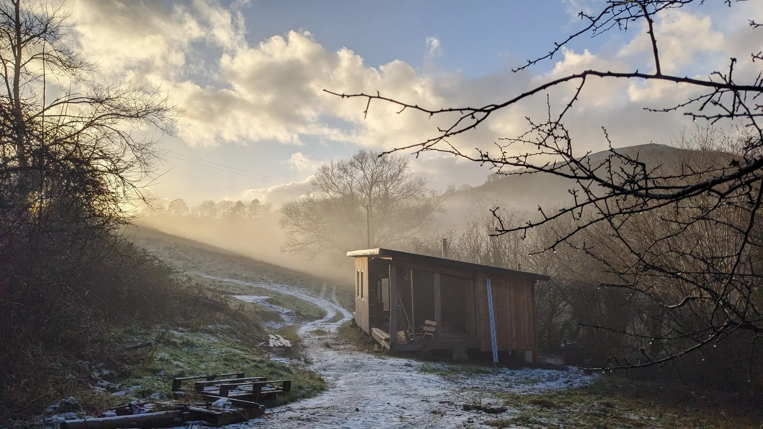 A magical shot of Ty Mawr the timber clad, flat roofed single storey communal building for the cabins and Onnen. Early morning winter sunshine with mist enveloping the scene, rising over the fields and horizon beyond Ty Mawr. The path curves gently o