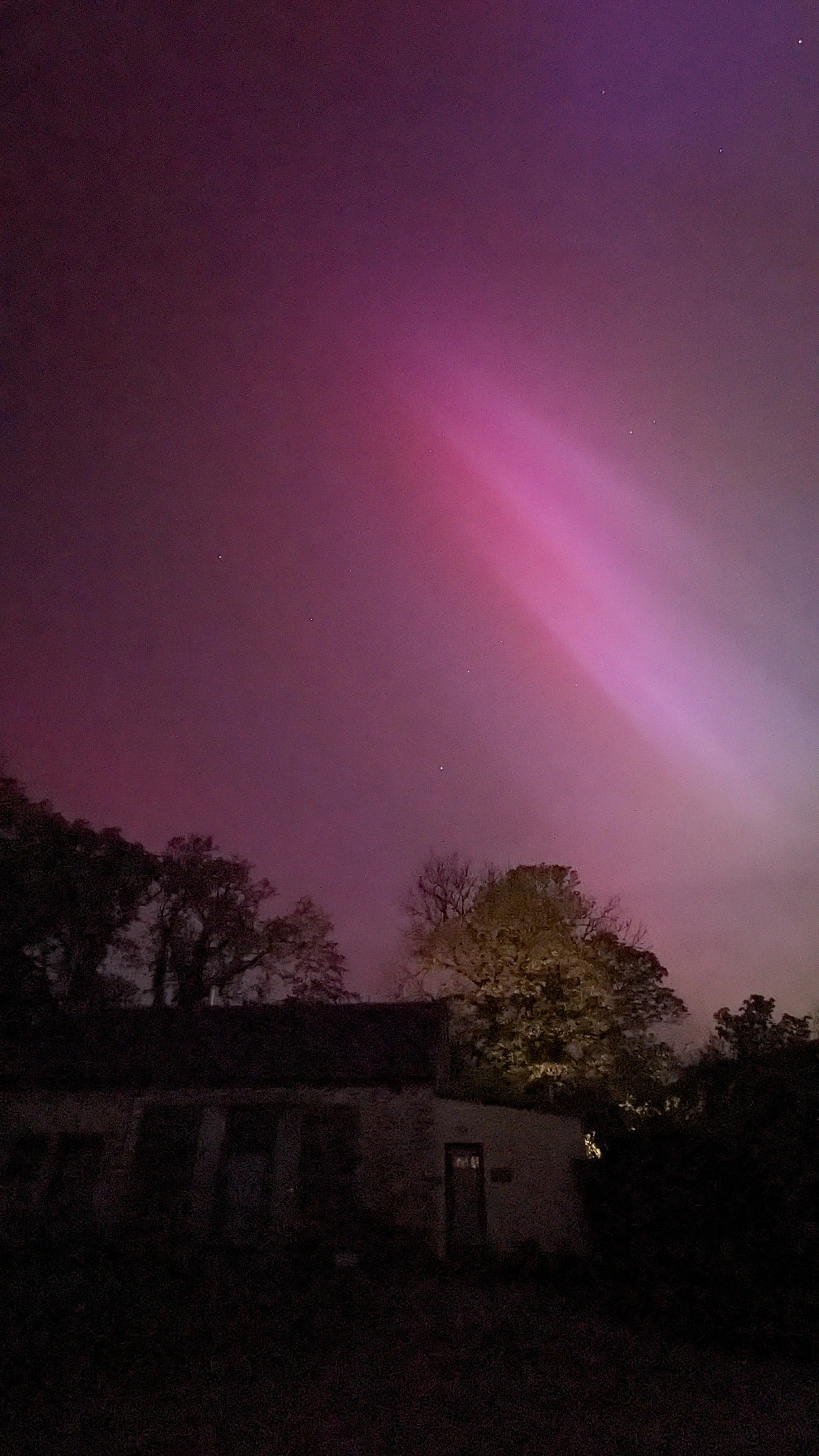 Purple pink columns of light known as the Northern Lights shown above the Barn at Llwynbwch Farm.