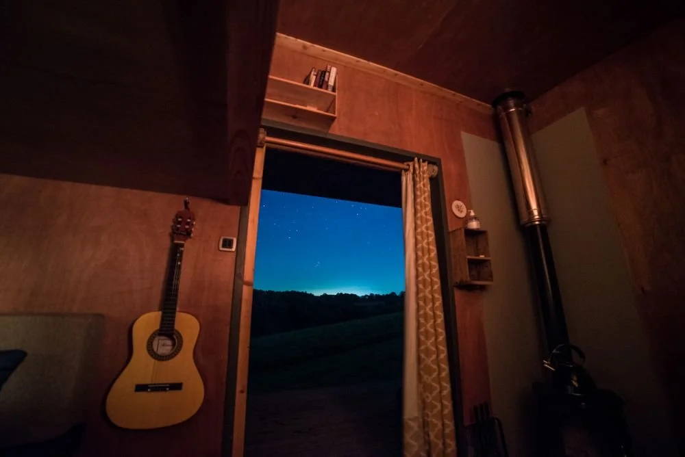 Looking through the doorway at Derwen cabin at night, framed by a guitar hanging up and the stove to the other side of the door.