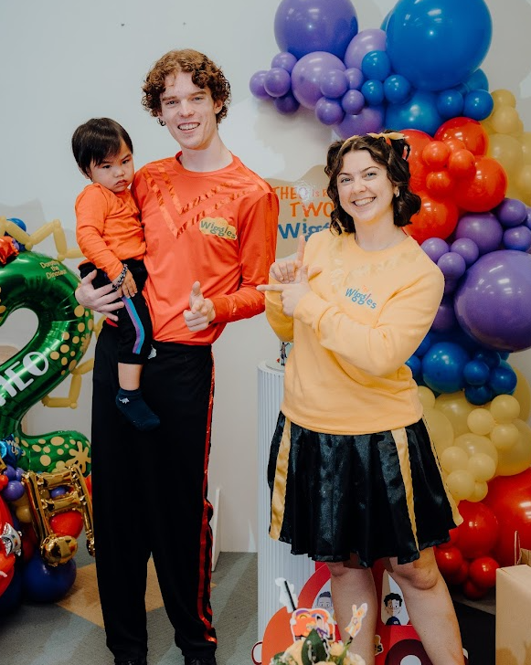 A woman and a man dressed as the Wiggles standing by some balloons