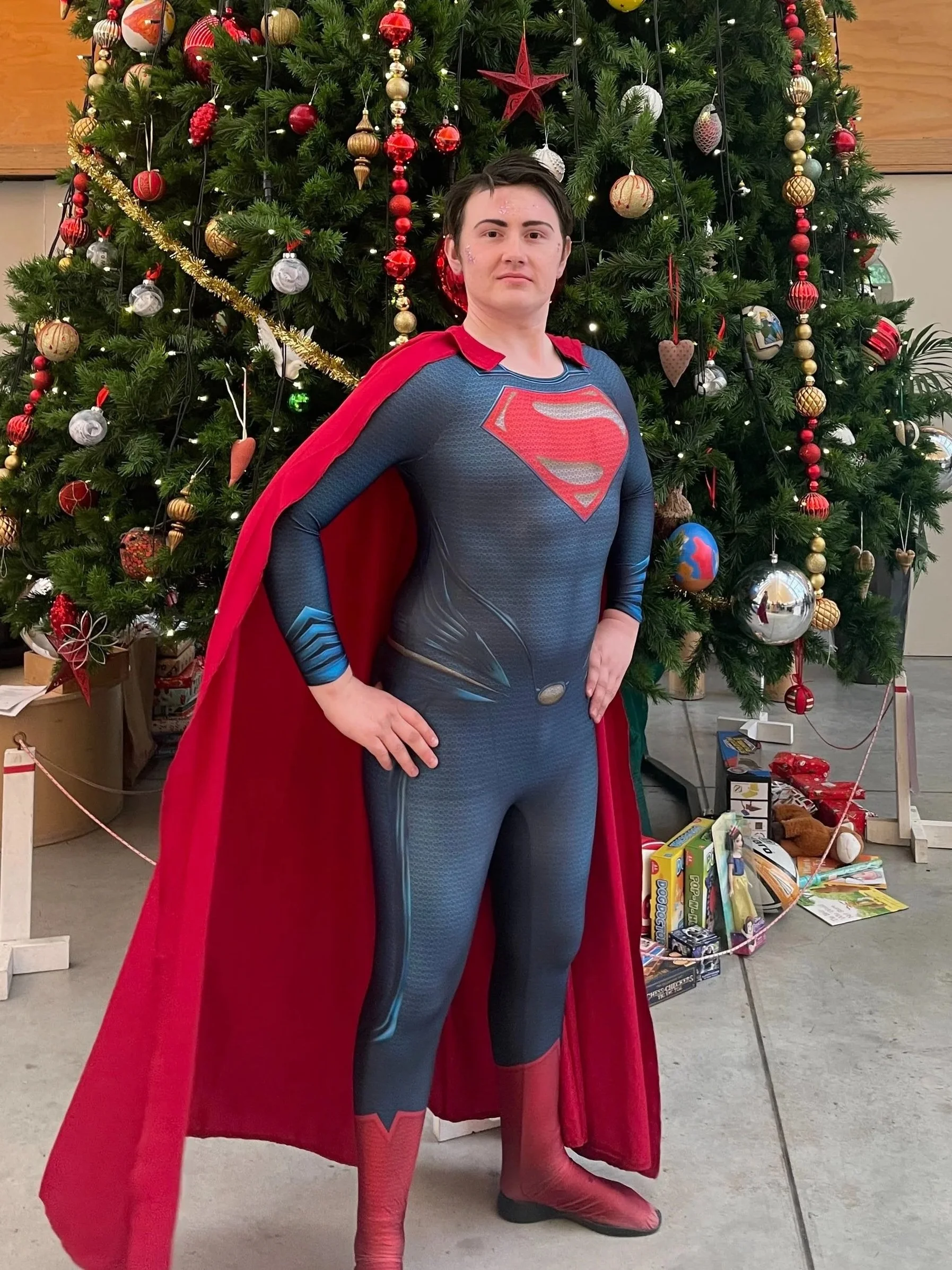 man dressd as superman at a market in front of a christmas tree