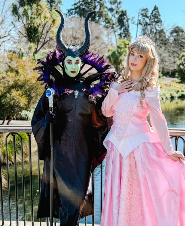 woman dressed as the evil maleficent and woman dressed as aroura outside on a bridge in the gardens