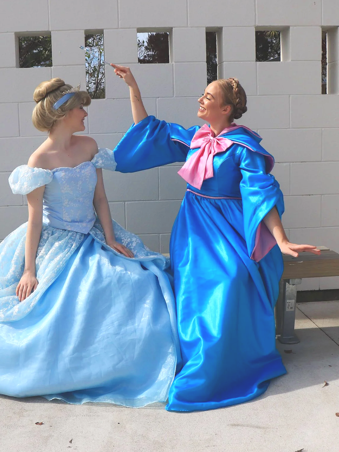 Person dressed in a bright blue gown with puffy sleeves and a pink scarf tied into a large bow around the neck, holding a sparkly Princess Peach wand from the Mario franchise.