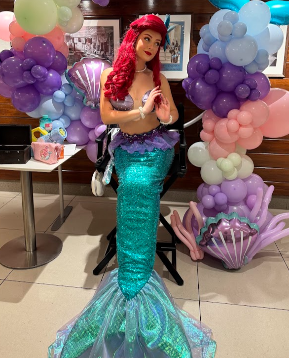 woman dressed as a mermaid with a mermaid tail and large prop form for her hair with mermaid colour  balloons 