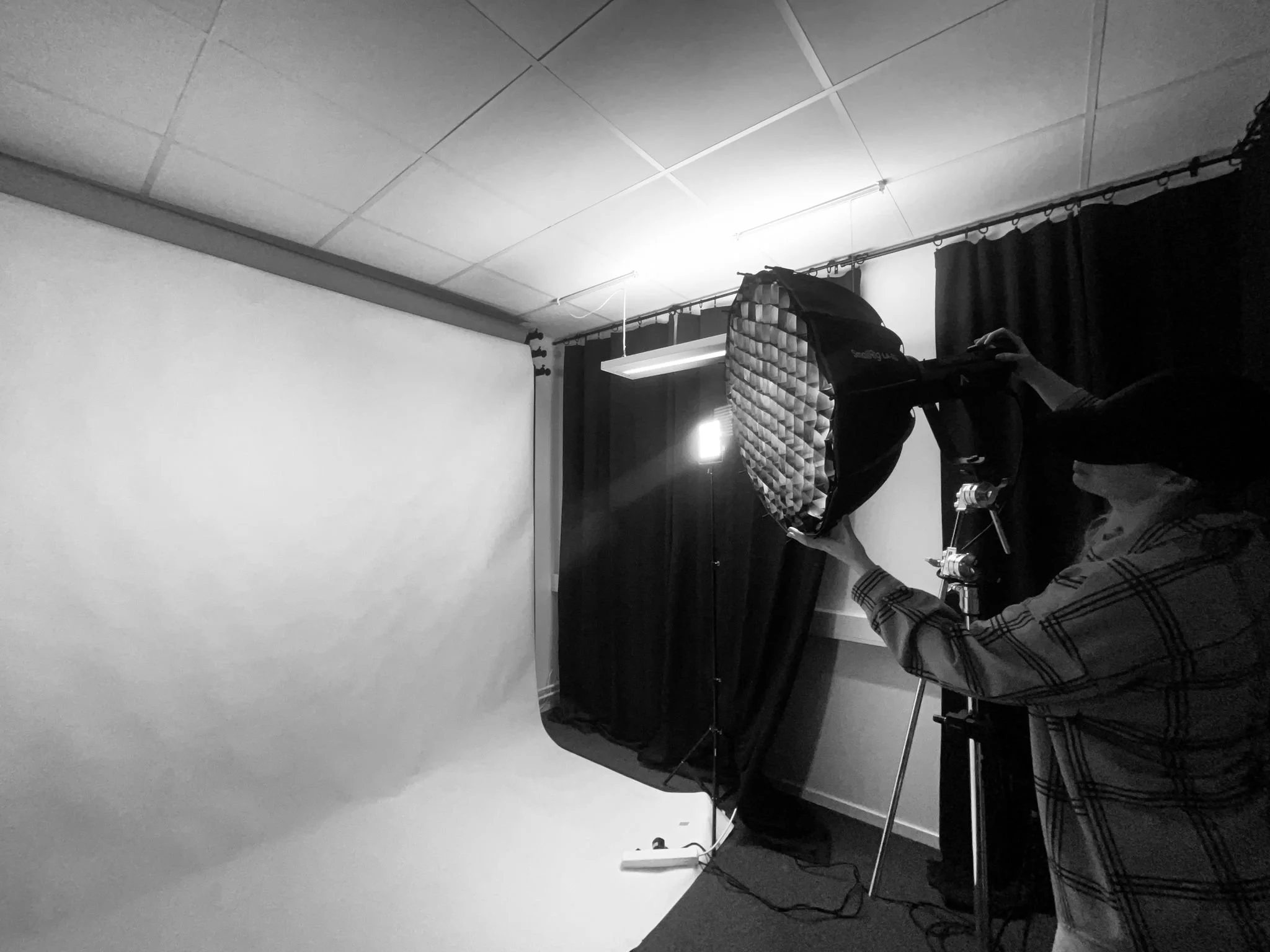 En person som justerar en fotografisk studioblixt framför en vit backdrop i ett fotostudio.