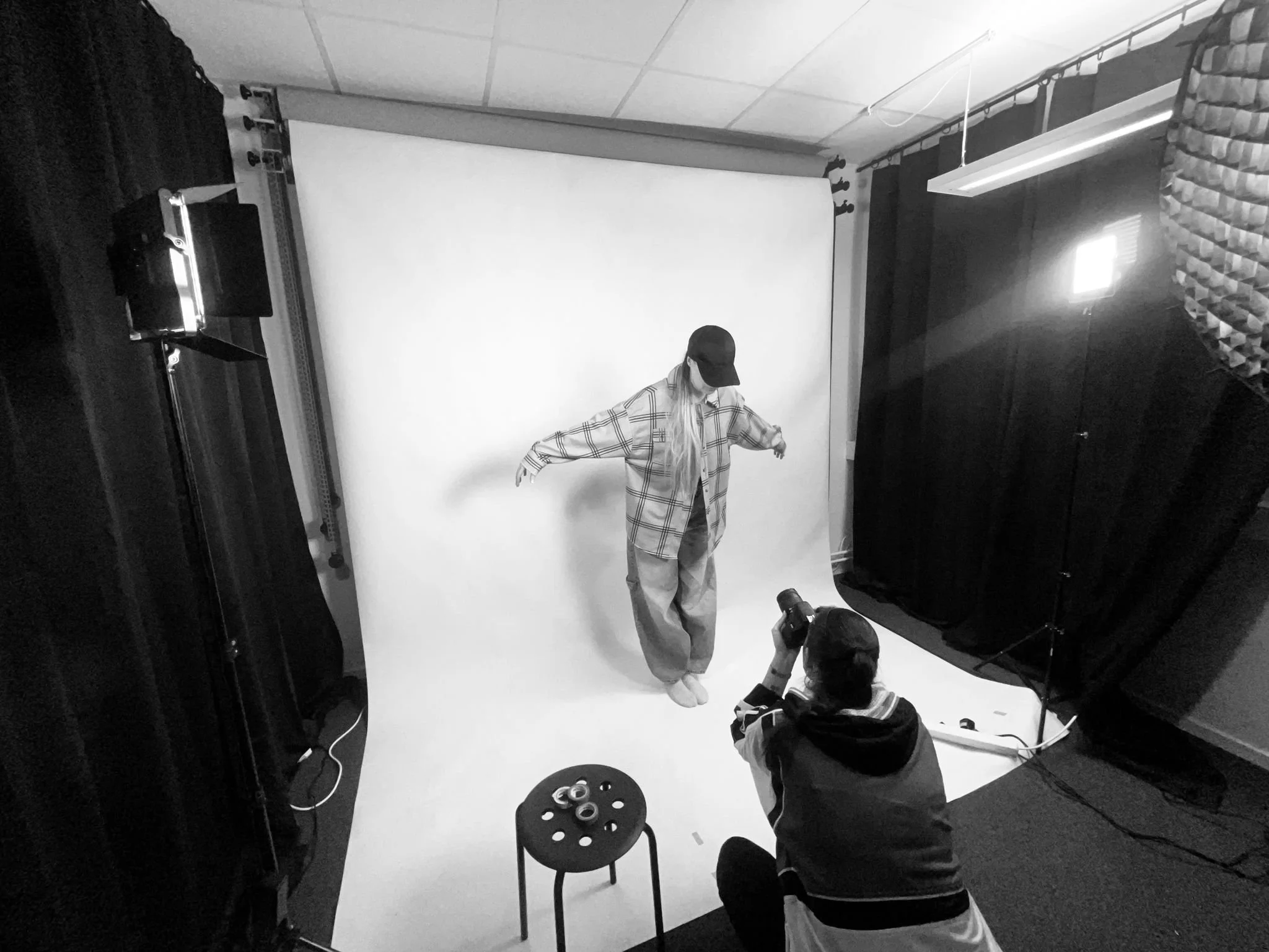 En person i en fotostudio tar en bild av en modell som poserar framför en vit bakgrund. En annan person fotograferar modellen.