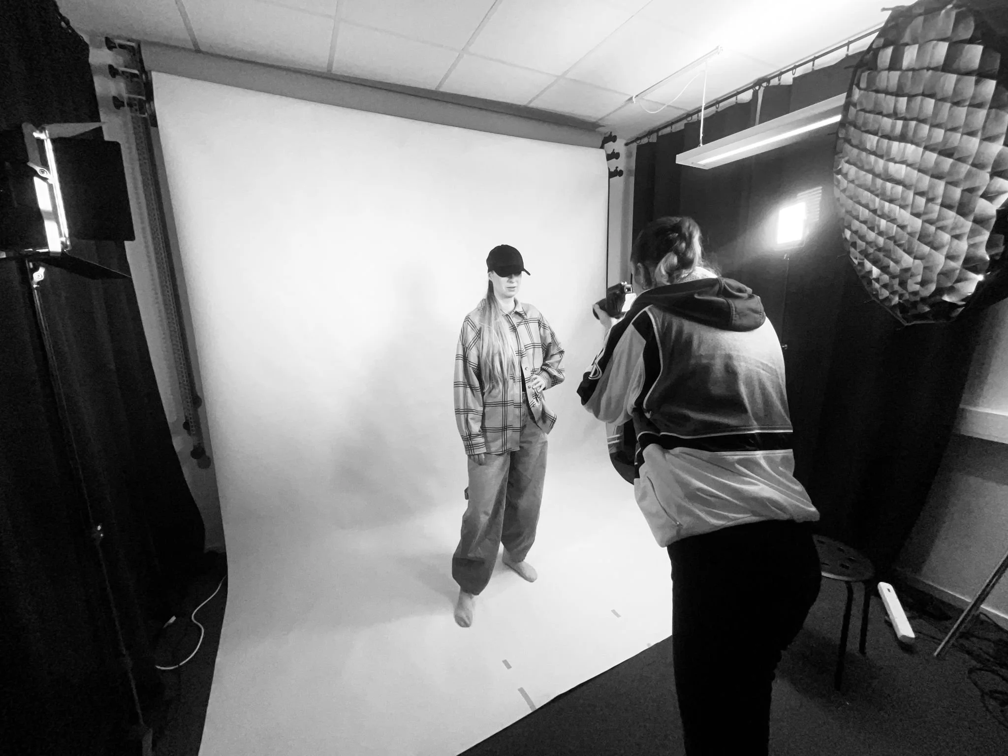 En person fotograferar en annan person i ett fotostudio med vit bakgrund.
