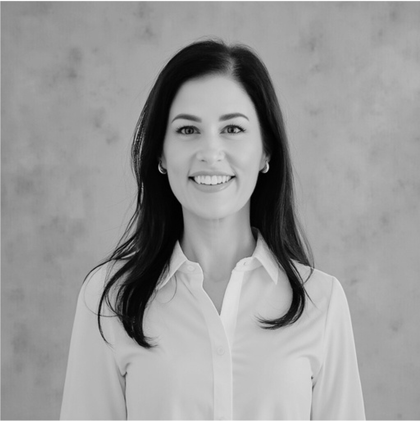 Black and white photograph of a woman with long dark hair, smiling, wearing a white collared shirt, in front of a plain background.