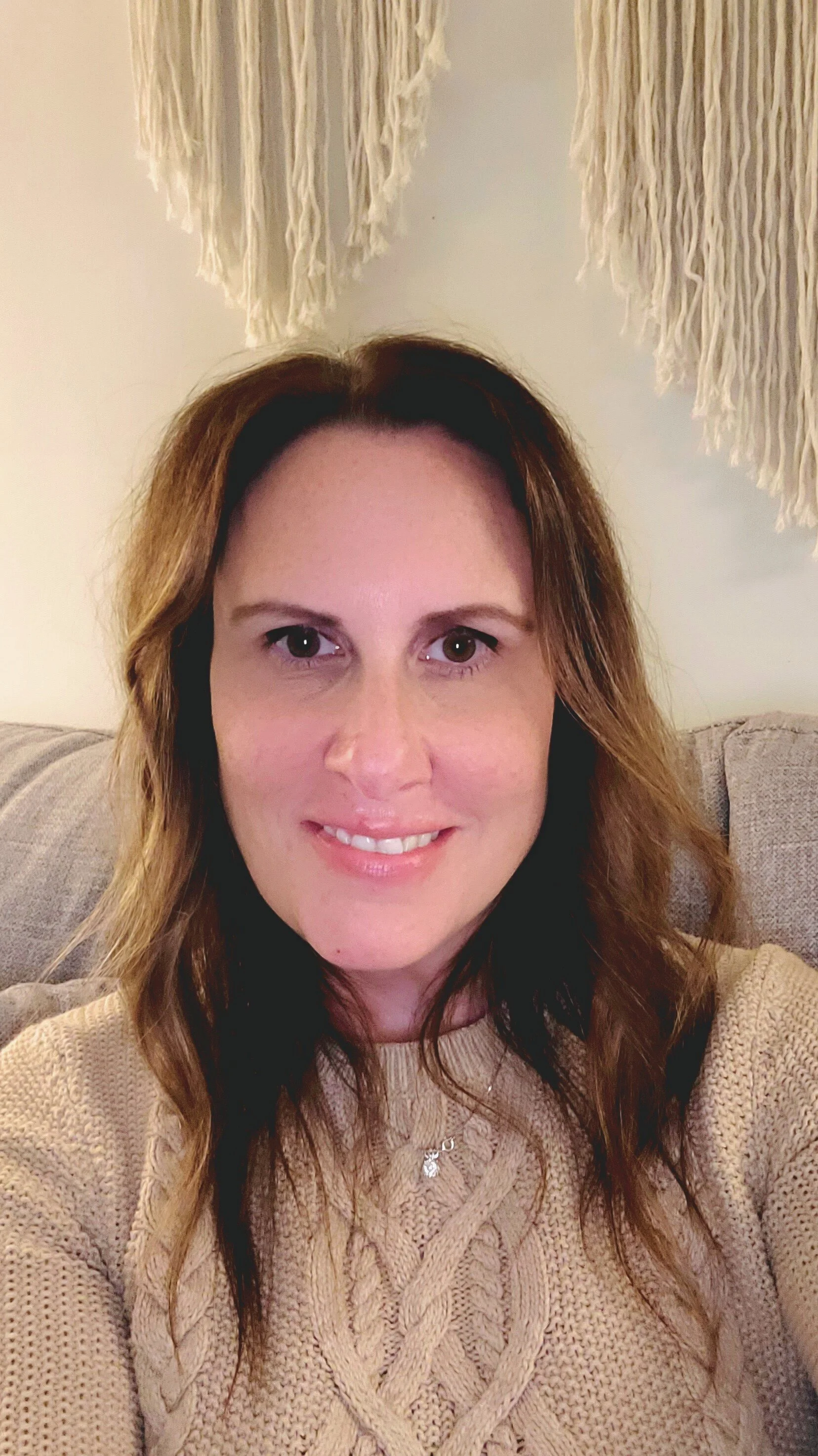A woman with shoulder-length wavy hair smiling, wearing a light-colored blazer over a dark top.