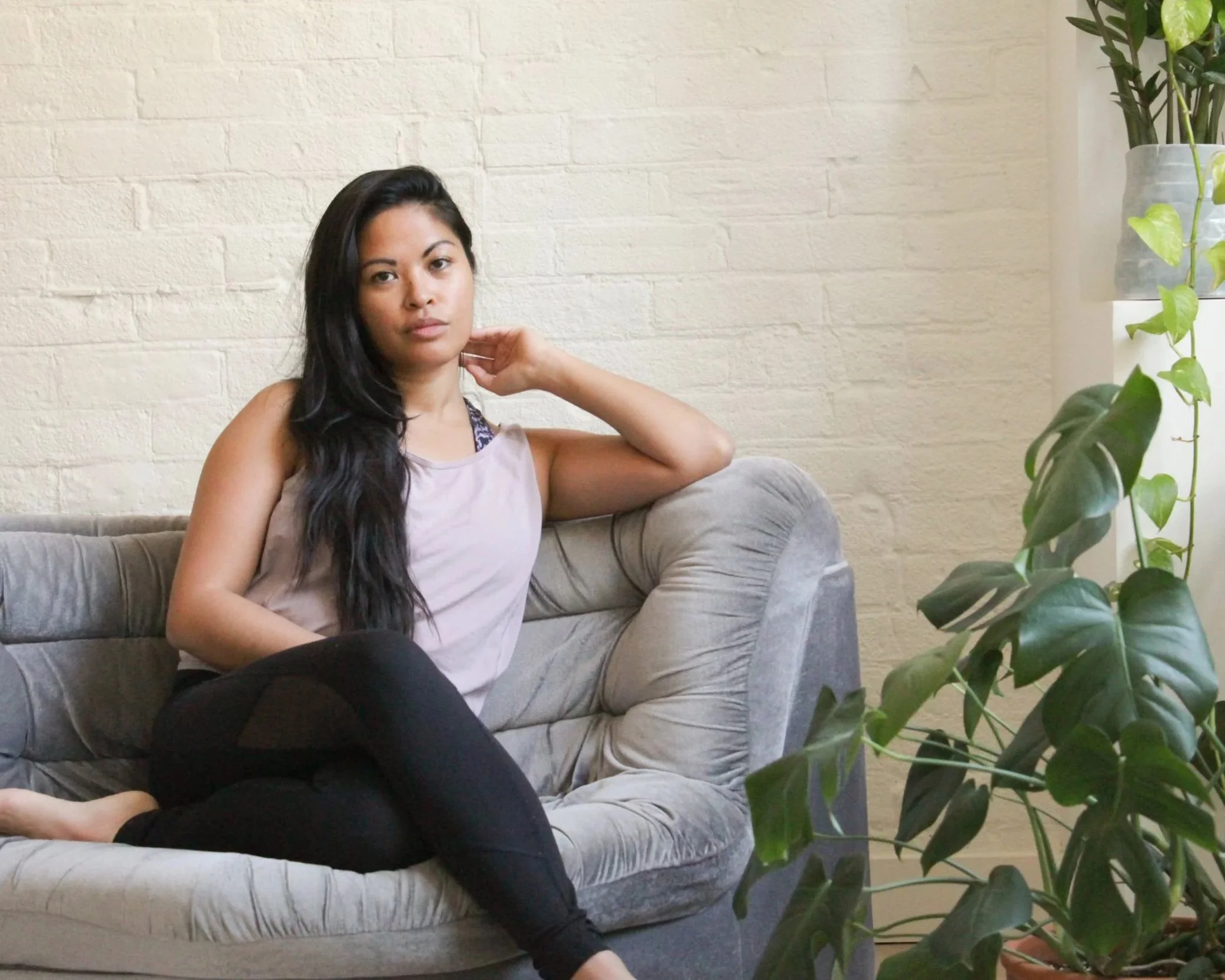 Person in black workout clothes sitting on a yoga mat, holding her foot with both hands, with a focus on her arms and hands, wearing bracelets.