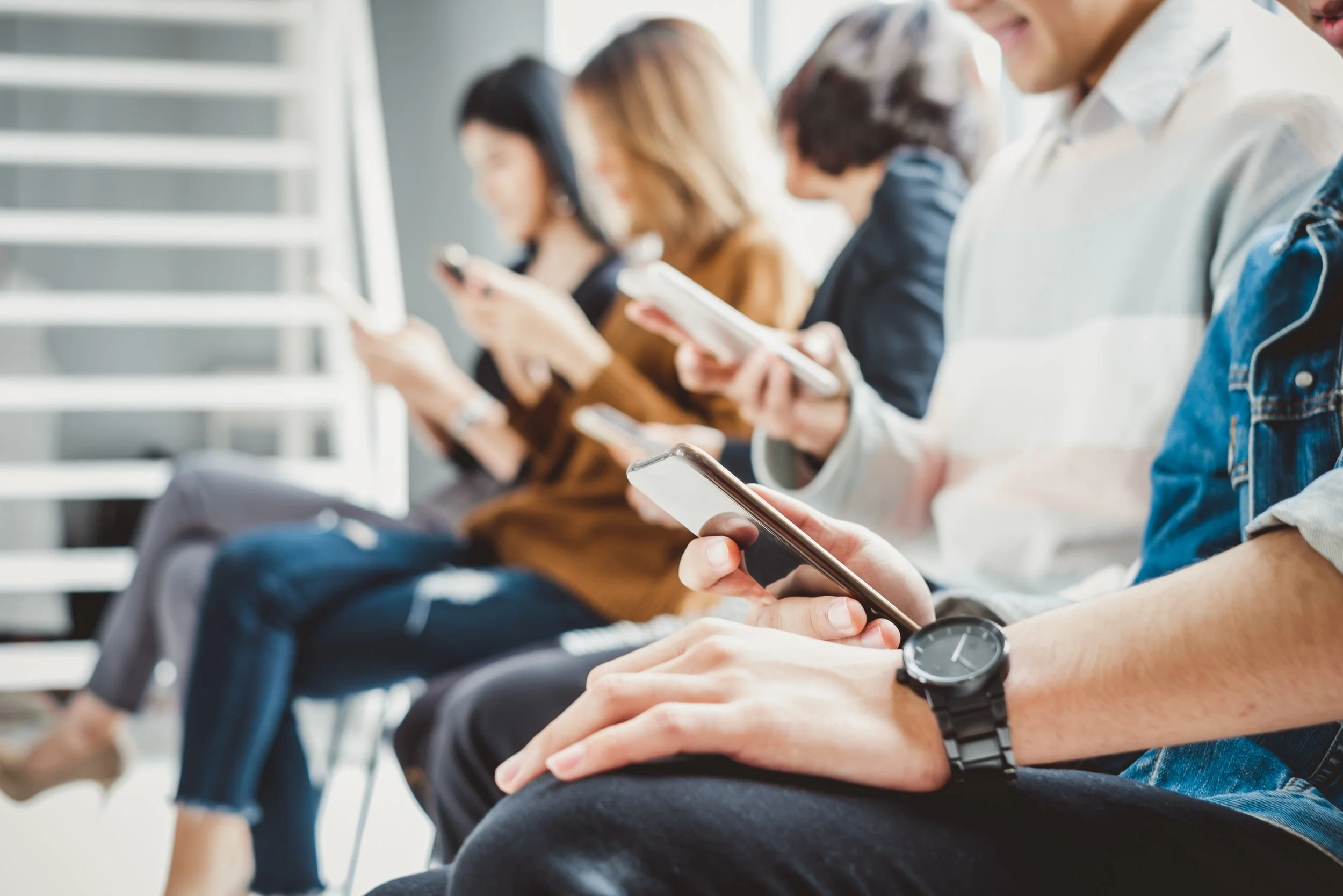 Multiple people sitting in a row, all looking at their smartphones.