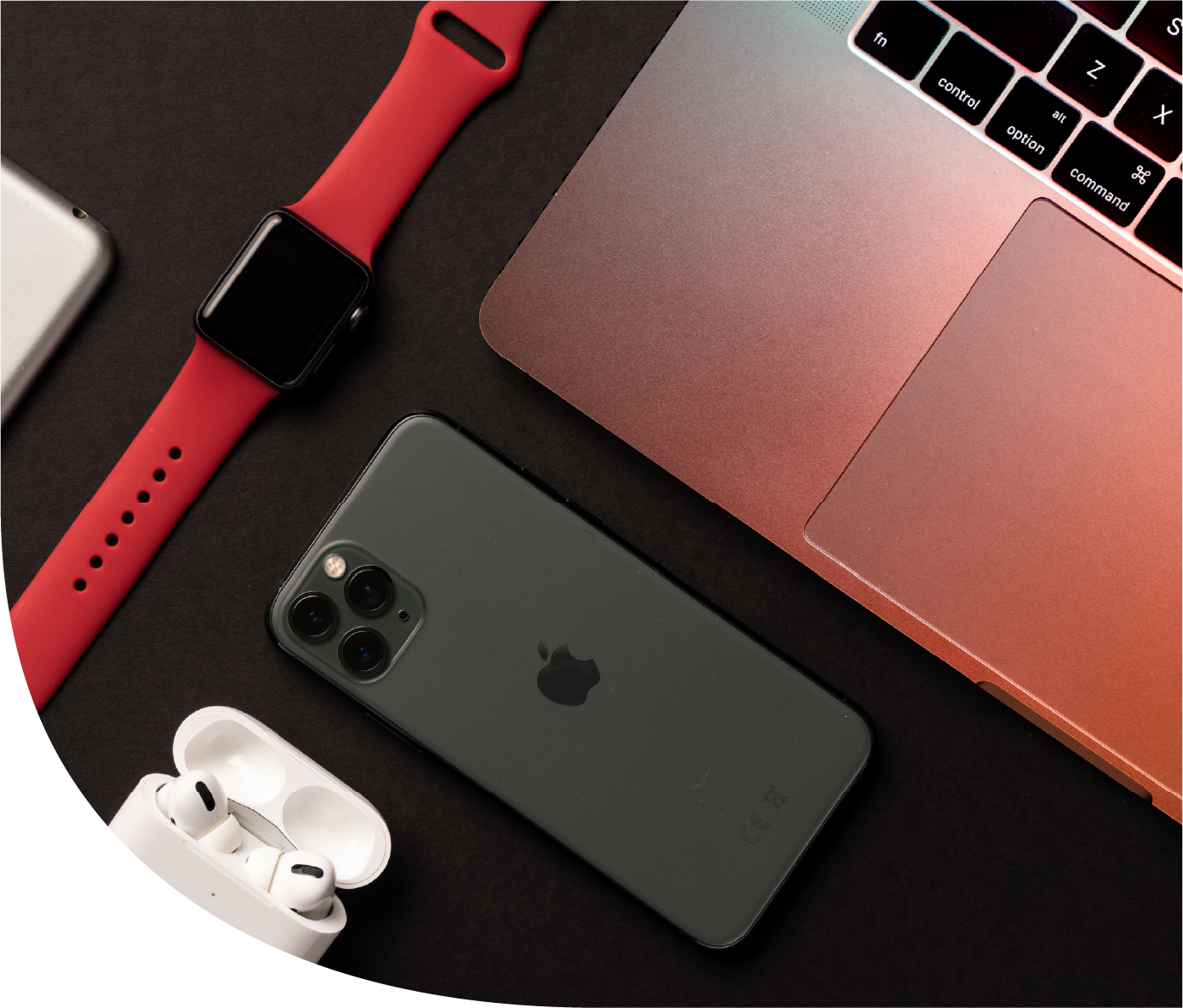 An iPhone with a triple camera, Apple AirPods in a charging case, an Apple Watch with a pink band, and a pink MacBook on a black surface.