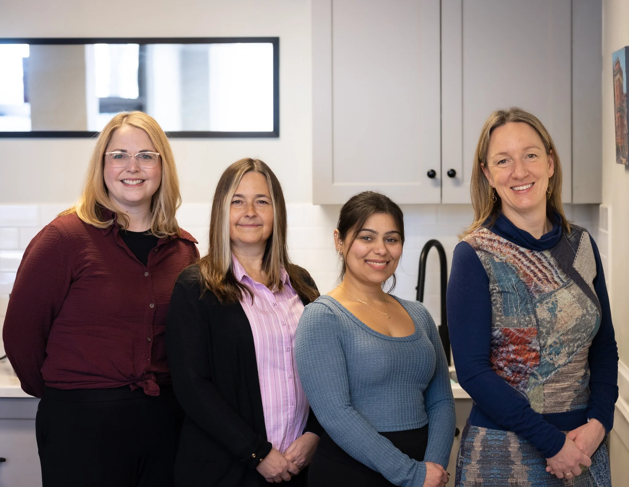 Four women standing in a kitchen, smiling at the camera.