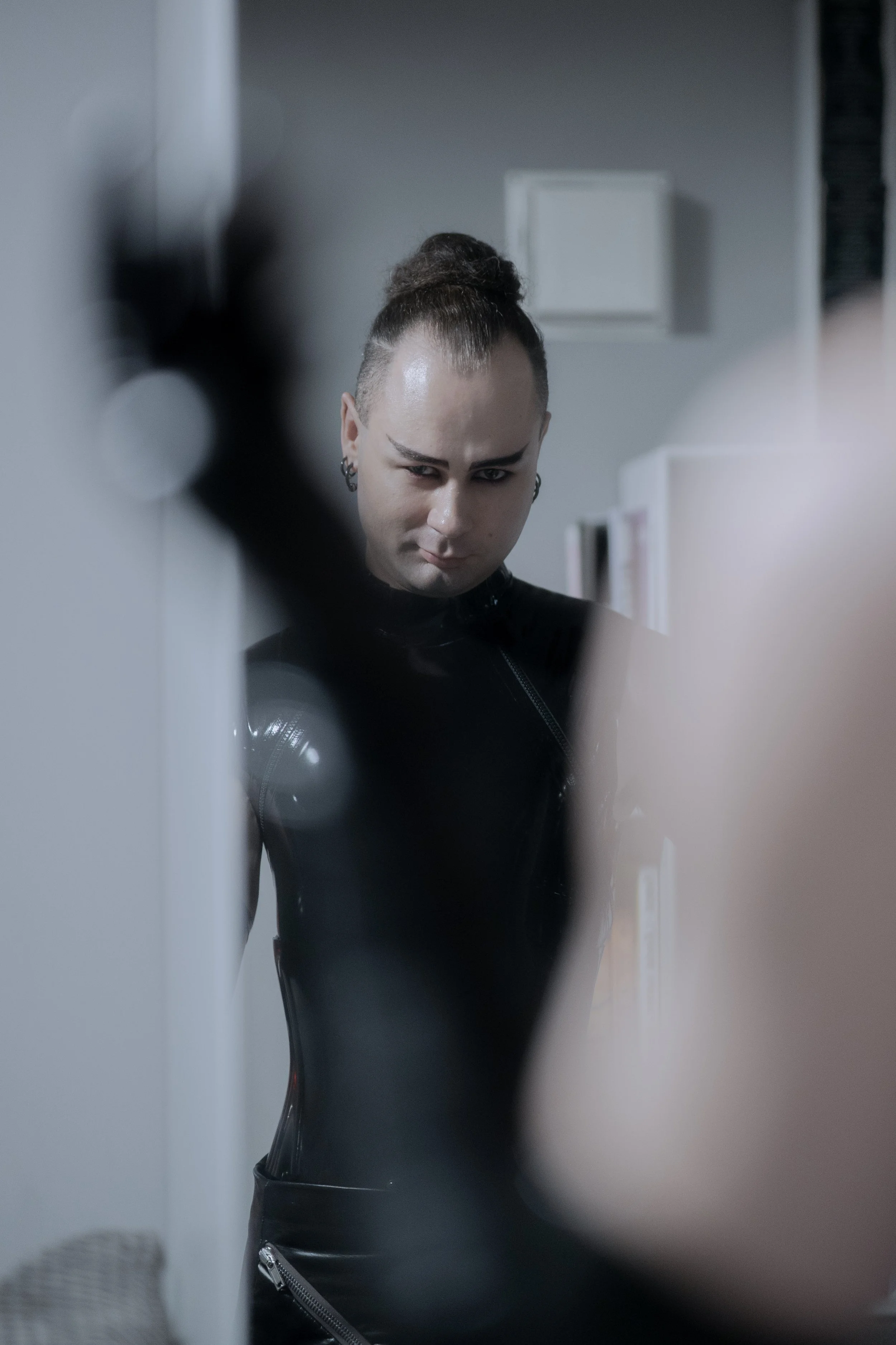 A Dominatrix standing in front of the mirror getting dressed in black latex with latex gloves.