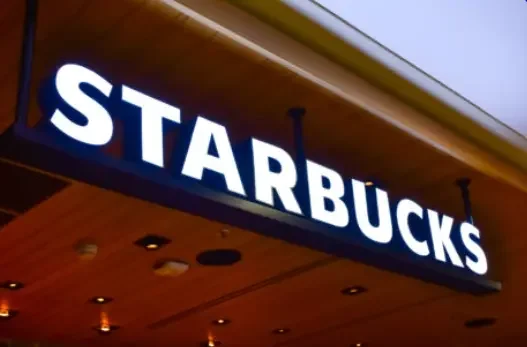 Starbucks store sign mounted on a wooden ceiling with lighting fixtures.