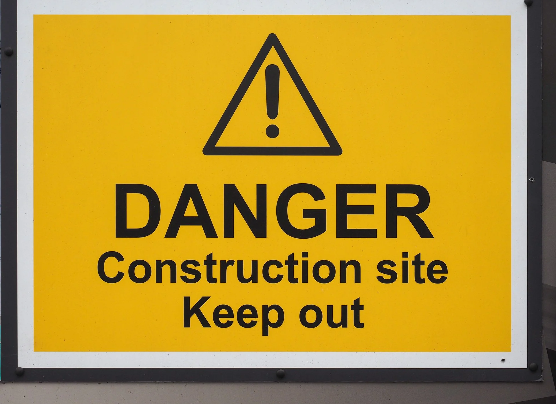 Yellow safety warning sign with black text that says 'Danger Construction site Keep out' and an exclamation mark inside a triangle.
