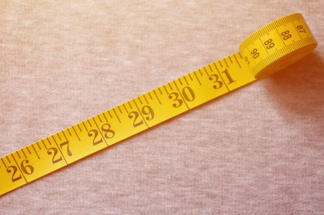 Yellow measuring tape stretched out on a beige surface, showing measurements from approximately 26 to 88 centimeters.