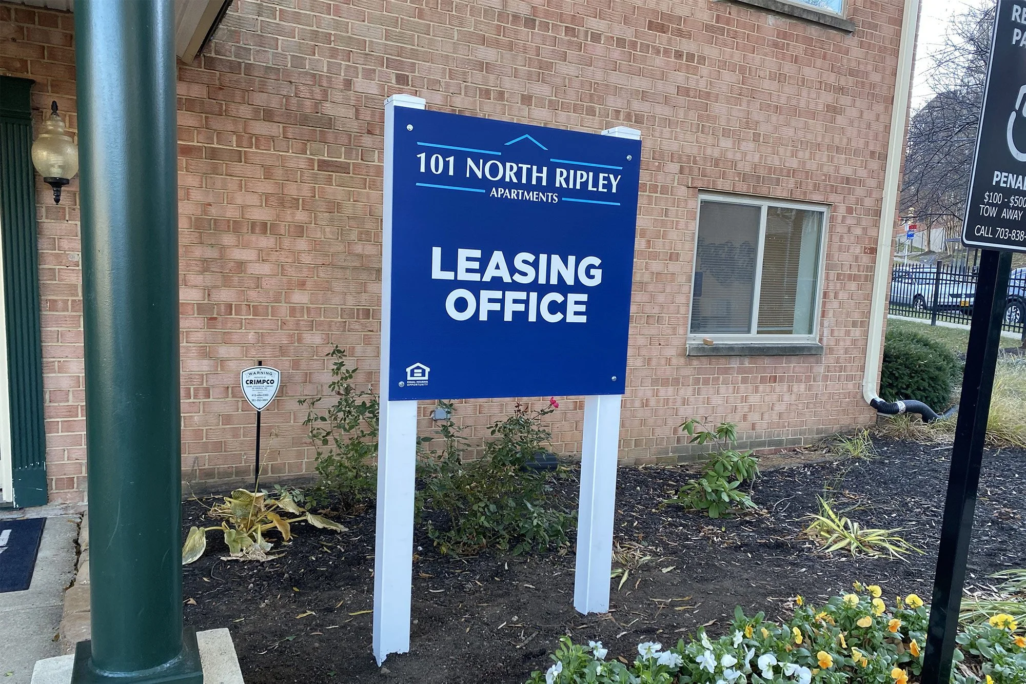 Blue sign with white text reading '101 North Ripley Apartments Leasing Office' in front of a brick building.