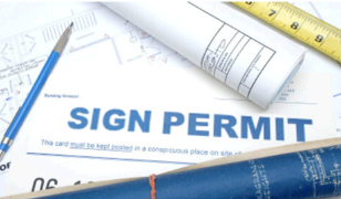 Sign permit application form with a pen, rolled blueprint, ruler, and a blue pencil on a desk.
