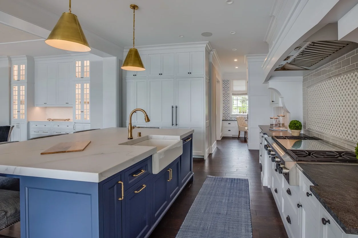 Modern kitchen with white and navy blue cabinetry, gold accents, and dark hardwood floors.