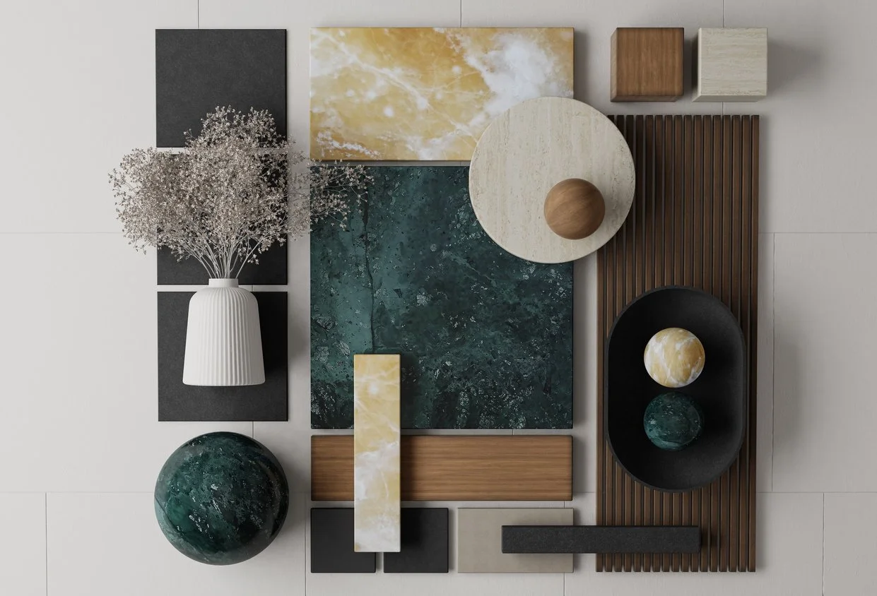 Arrangement of various decorative objects and materials, including a white vase with dried flowers, painted wood, marble, and textured panels in black, beige, yellow, green, and brown, displayed on a flat surface.