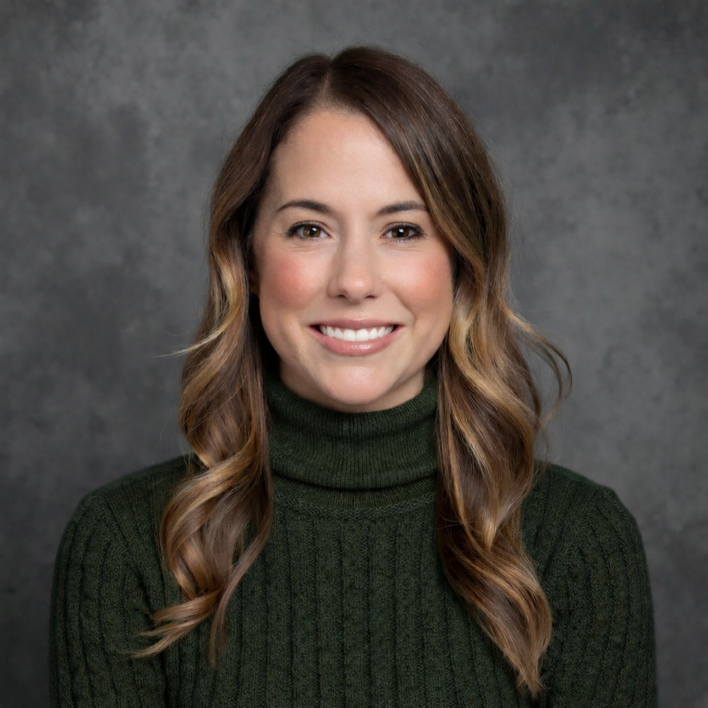 Portrait of a woman with long wavy brown hair wearing a dark green turtleneck sweater, smiling against a gray textured background.