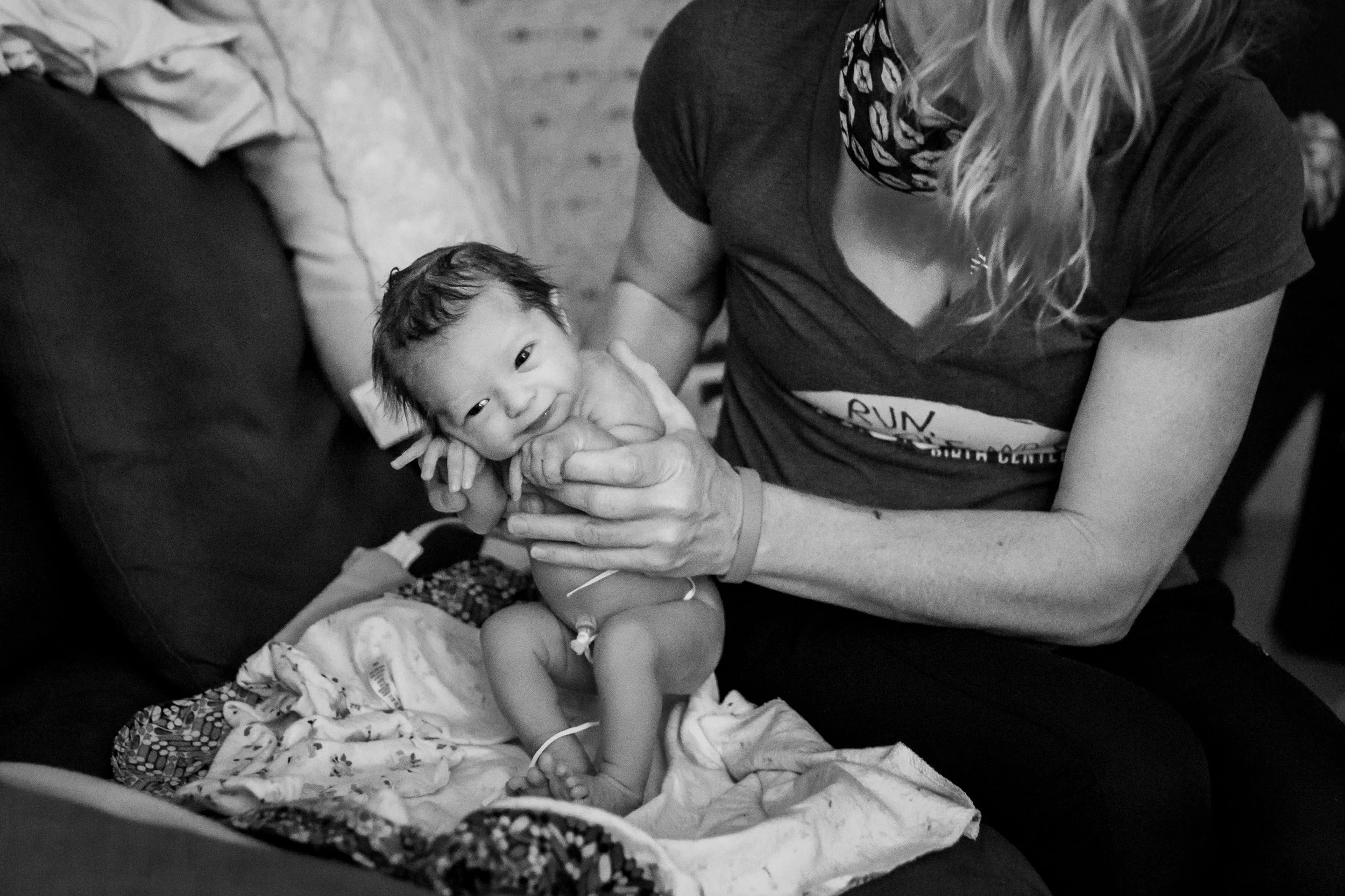A woman holding a young child, who is sitting on a blanket on a couch, with medical wires attached to the child.