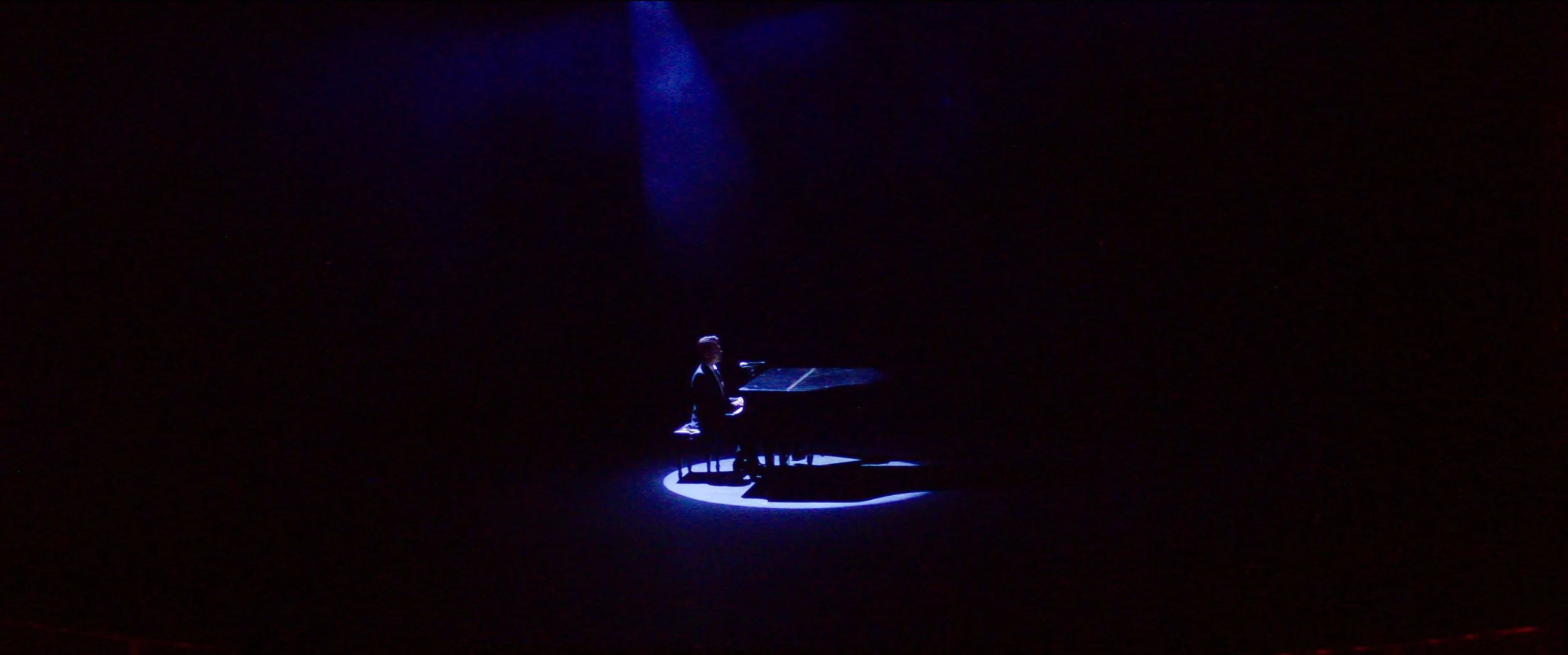 A person playing a grand piano on a dark stage with a spotlight highlighting them and the piano.