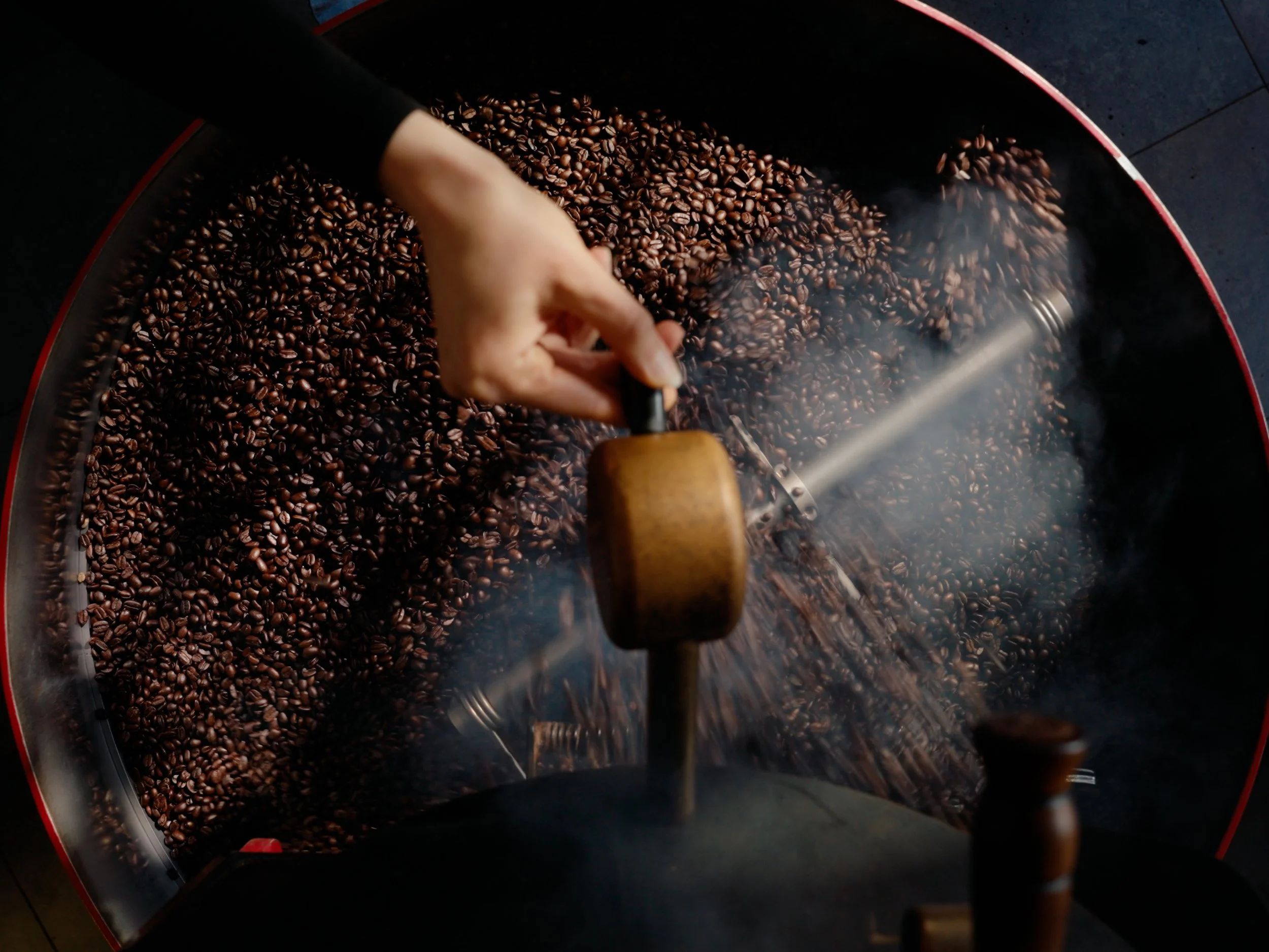 A hand stirring roasted coffee beans in an industrial coffee roasting machine.