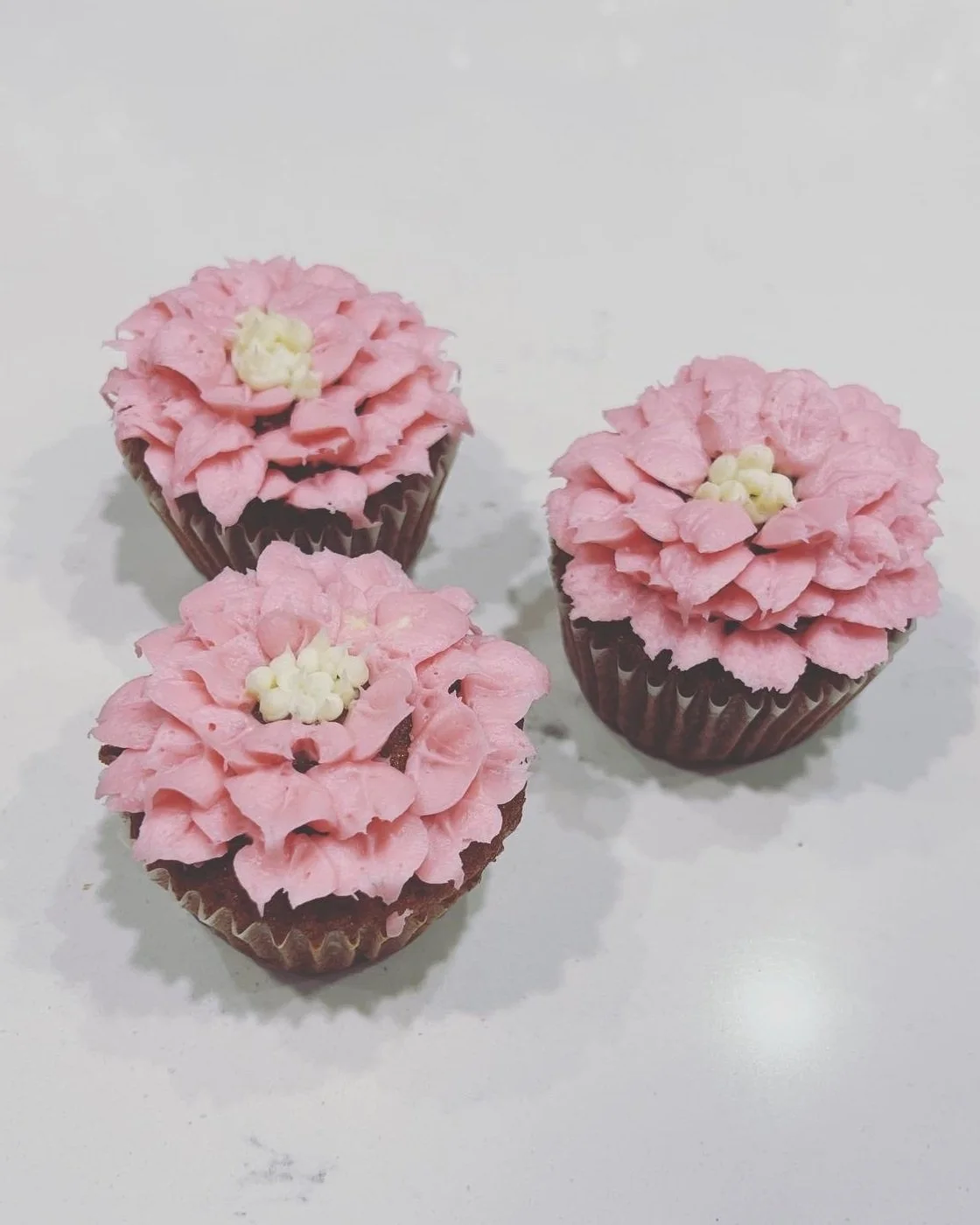 Three cupcakes decorated to look like pink flowers with white centers, on a white surface.