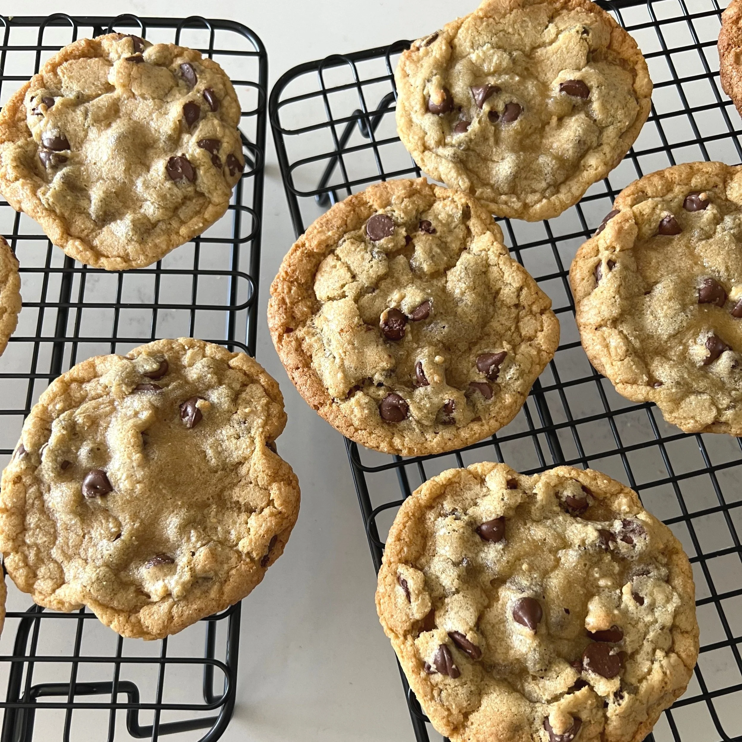 Freshly baked chocolate chip cookies cooling on black wire racks.