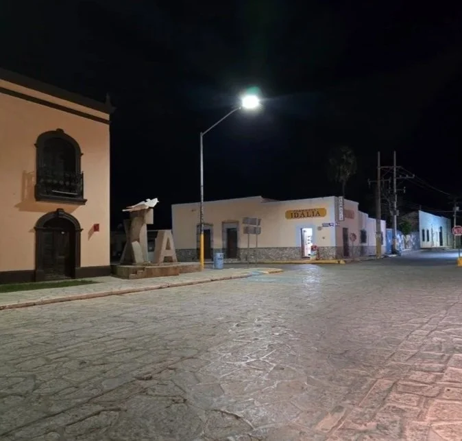Calle vacía de noche con edificios, incluye una fuente y una lámpara iluminando