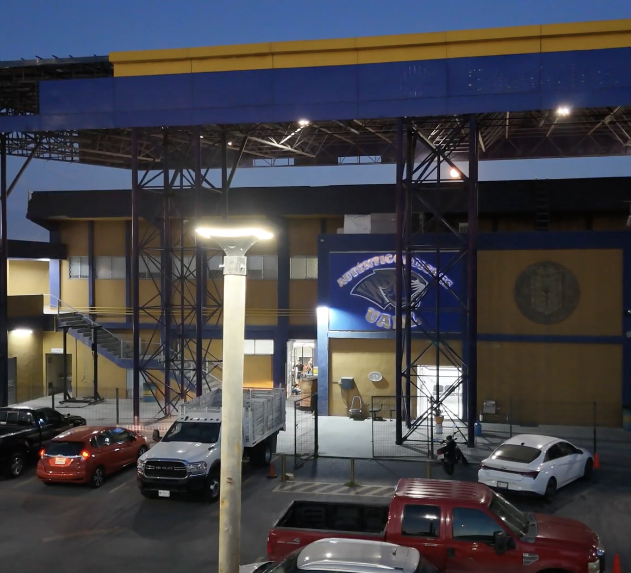 Estadio con vehículos estacionados frente, estructura de acero y logo de los Atléticos de Oakland en la pared.