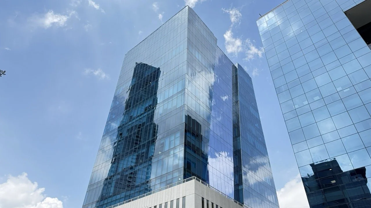 Edificio de oficinas moderno con fachada de vidrio reflejando el cielo y nubes.