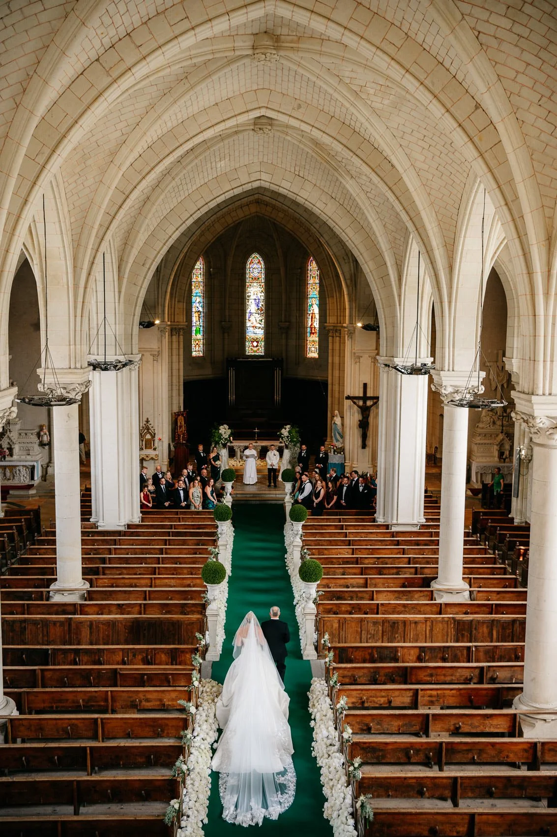 A wedding ceremony inside a church with a bride walking down the aisle towards the altar, where guests and the officiant are gathered.