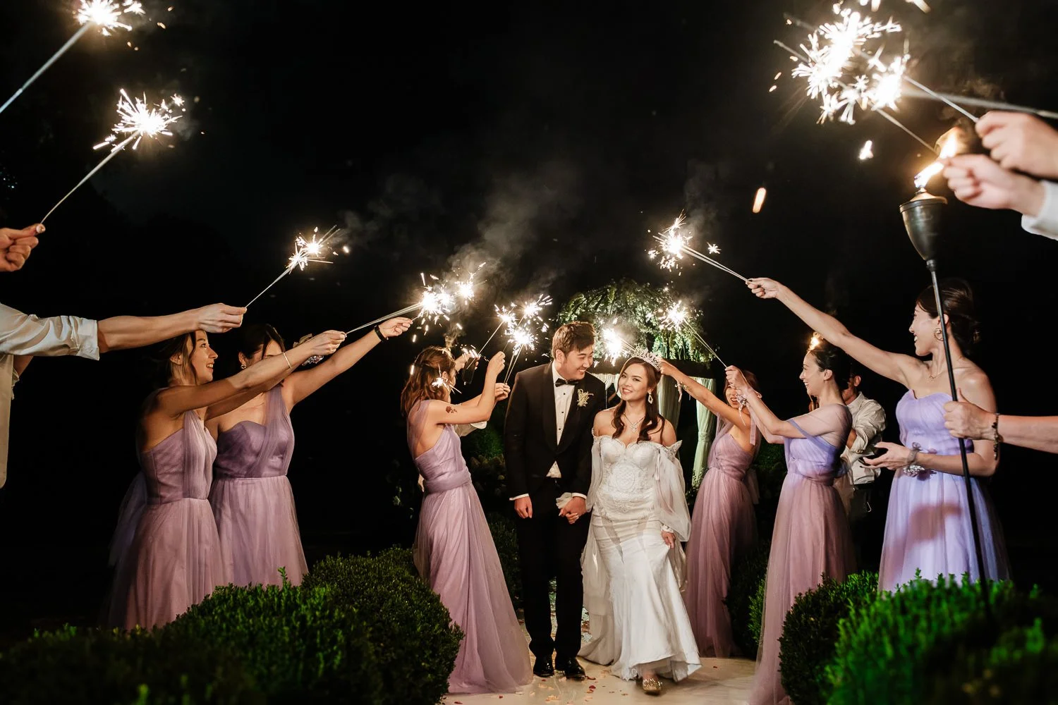 A wedding celebration with the bride and groom walking under sparklers held by friends and family at night.