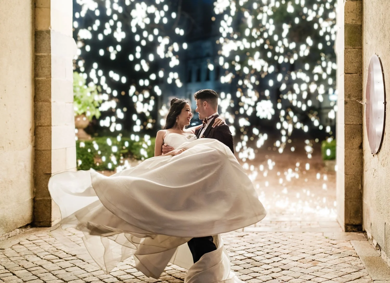 A bride and groom dance in a stone archway with a night sky and illuminated decorative patterns in the background.