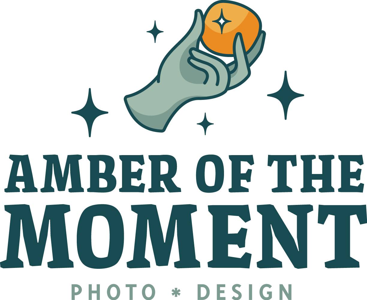 Logo for Amber of the Moment featuring a stylized hand holding an amber gemstone with sparkles, with text 'Amber of the Moment' and 'Photo Design' underneath.